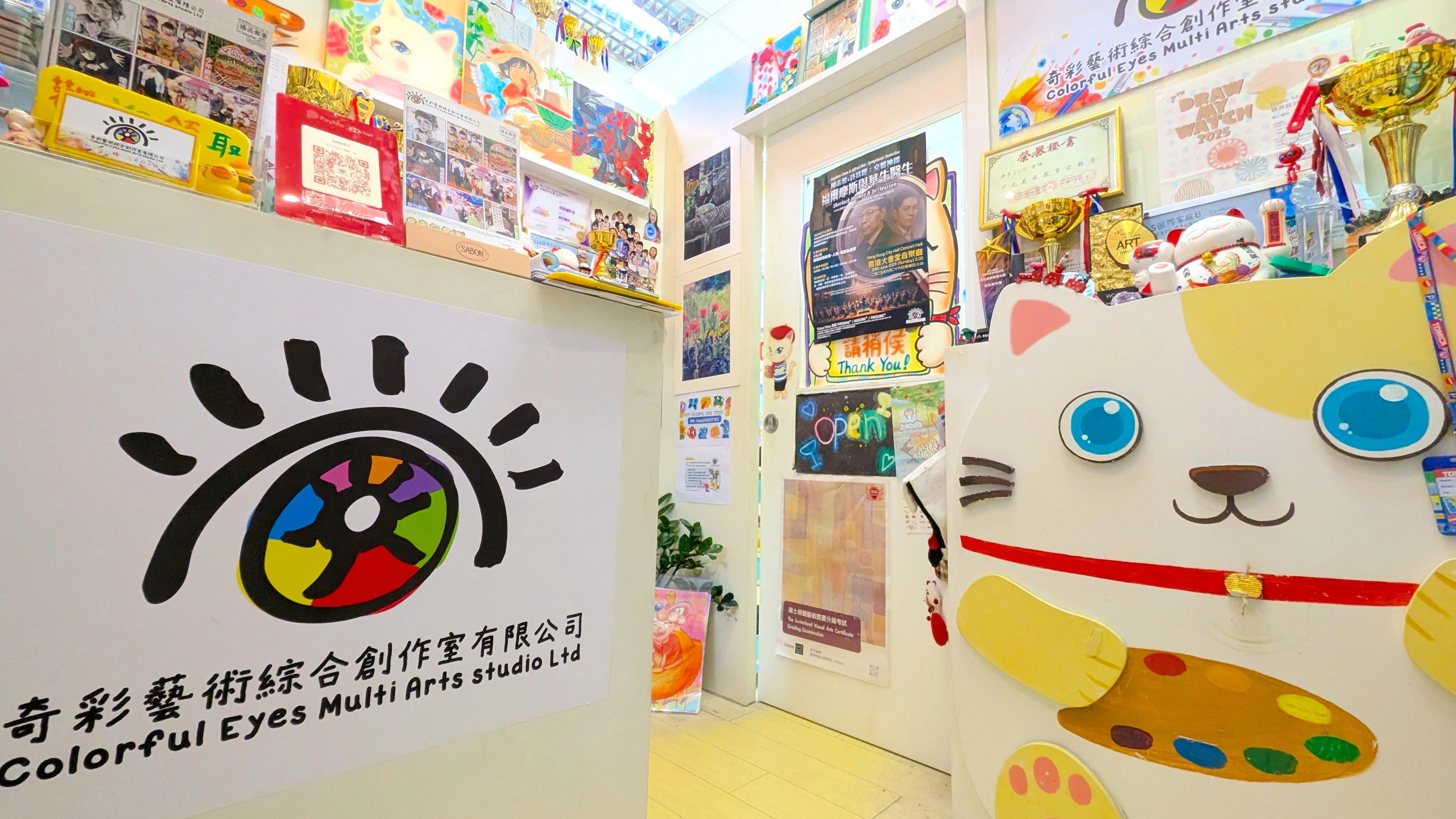 明亮寬敞的創作空間：室內光線充足，配備整潔舒適的木製畫桌與色彩繽紛的座椅，營造出輕鬆愉快的學習氛圍，讓孩子能專注於藝術創作。  豐富的學員作品與榮譽展示：牆面上掛滿了學生們充滿童真與創意的多元畫作、素描及手工作品；櫃頂則整齊排列著大大小小的獎杯與獎項，見證了學員們在各大美術賽事中的優異表現。  完善的繪畫與手作設施：畫 - 奇彩藝術綜合創作中心